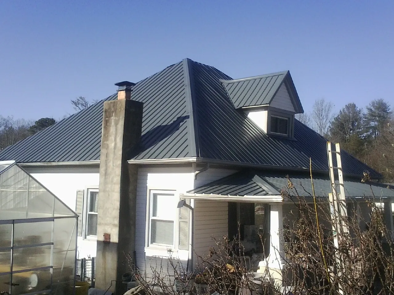 Dark blue standing seam metal roof on a white farmhouse with dormer — Slate & Tile Roof Repair by Roofing Brothers in Padroni
