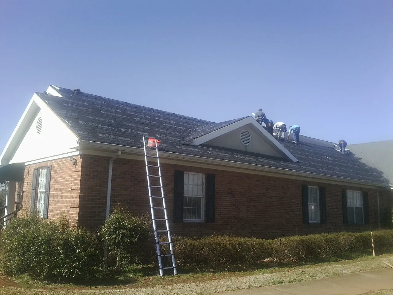 Crew tearing shingles off a brick ranch roof with a ladder set — Metal Roof Repair work by our crew in Padroni