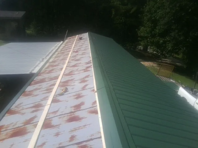 Old rusted panels beside newly installed green metal roofing — Wind Damage Roof Repair by Roofing Brothers in Padroni