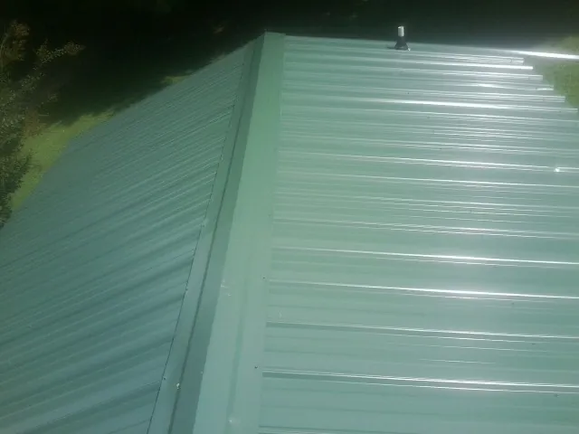 New green metal panels meeting at the ridge of a roof — Flat Roof Repair work by our crew in Padroni
