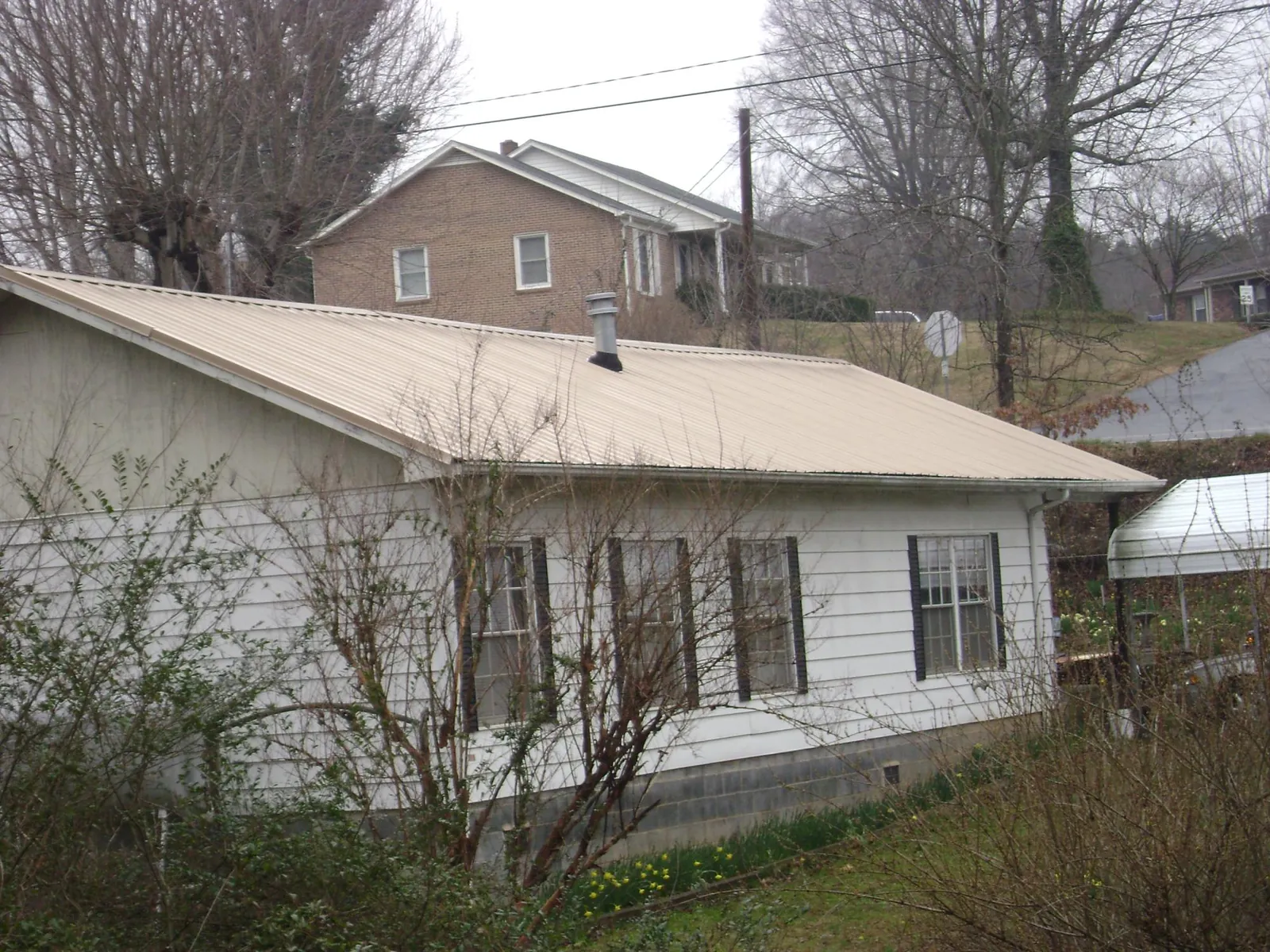 Tan metal roof on a white sided house set into a hillside — Commercial Roofing by Roofing Brothers in Padroni