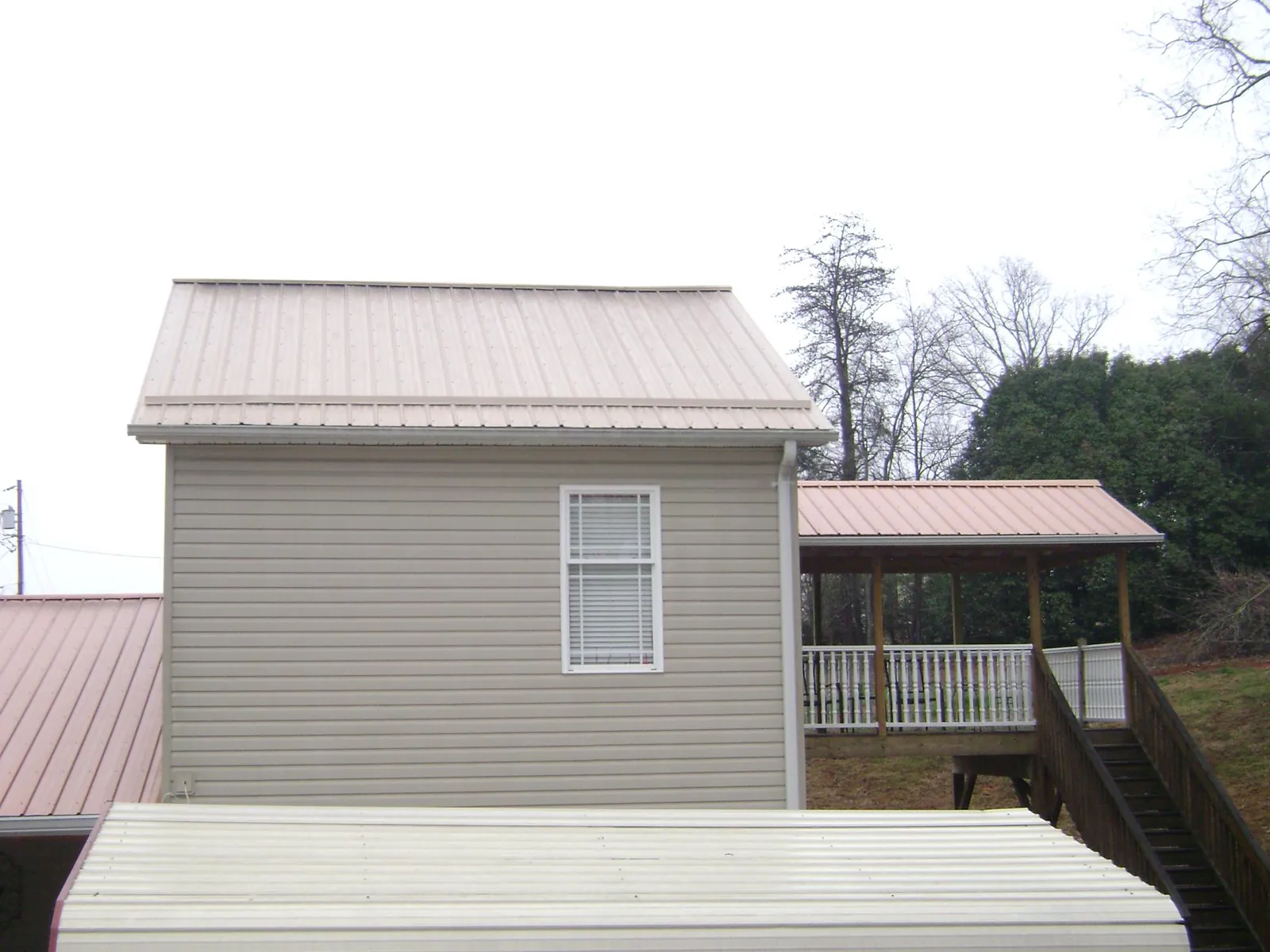Tan metal roofs on a two story addition and attached porch, from a Roof Replacement job in Padroni